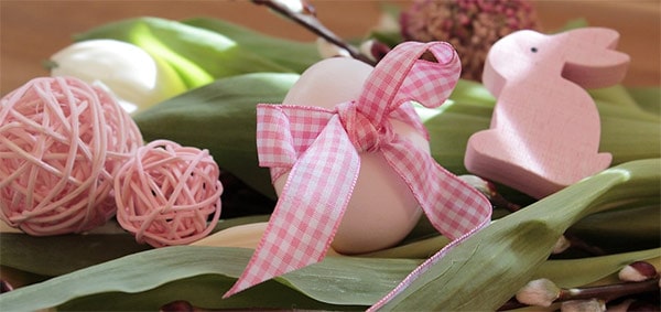 Pastel pink Easter egg tied with gingham ribbon, and a pale pink bunny rabbit on green leaves